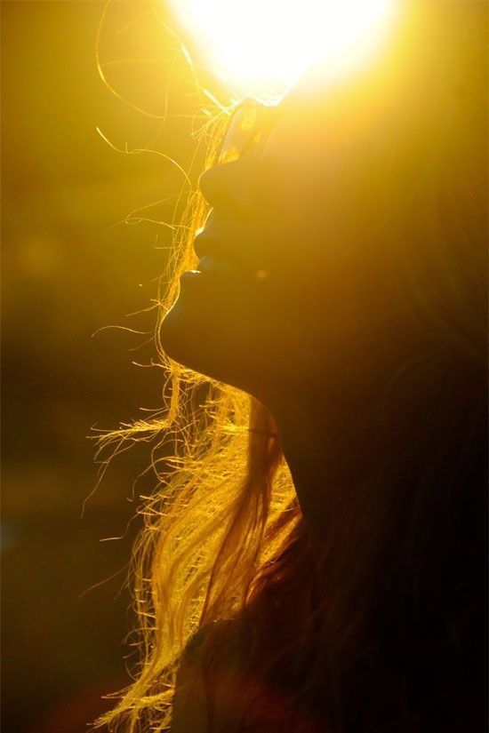 A woman&rsquo;s face lifted into low golden sunlight, her hair lit from behind
