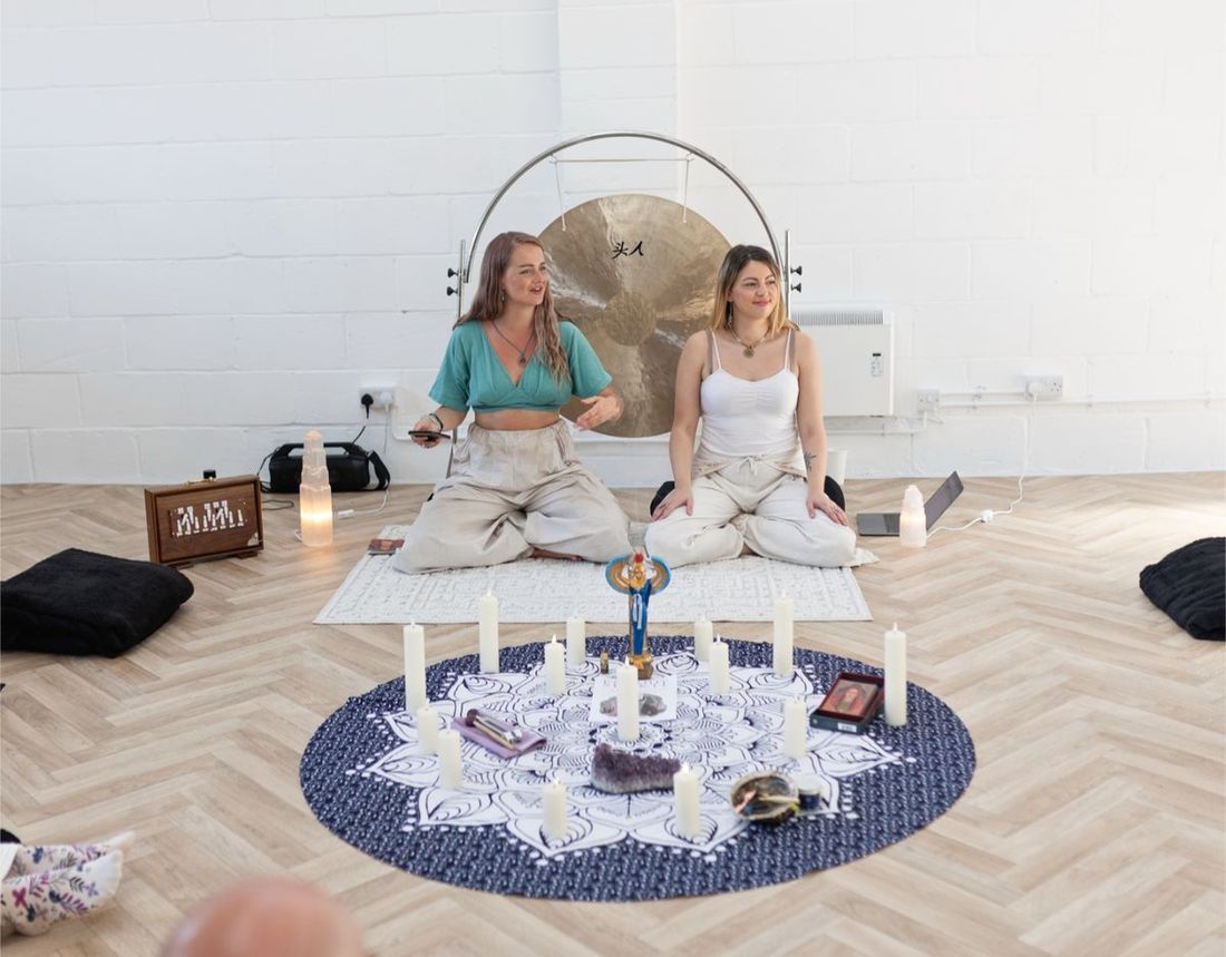 Maia and a co-facilitator seated by a gong beside a candlelit altar before a ceremony