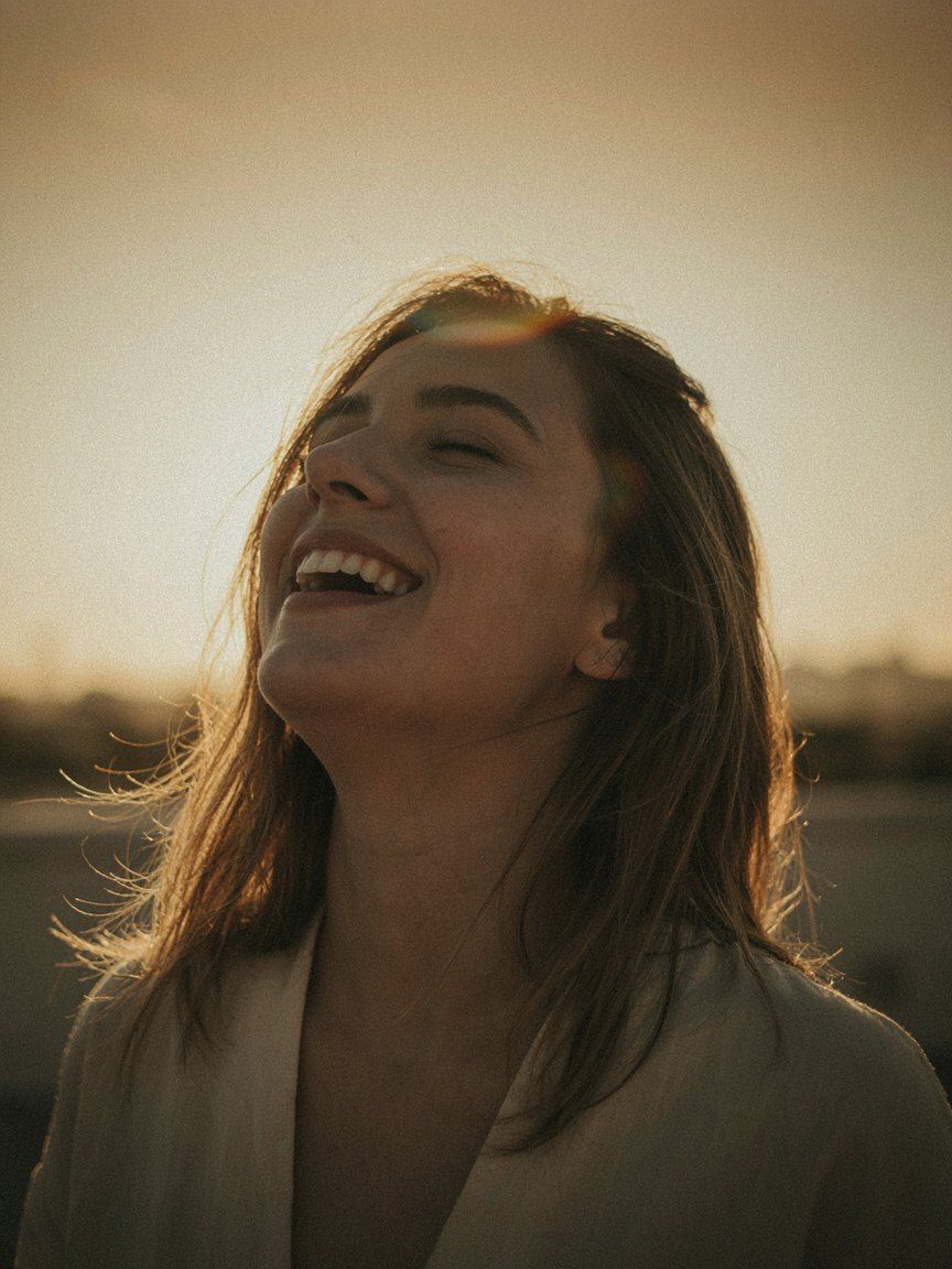A woman laughing with her head tipped back, low golden sun blazing through her hair