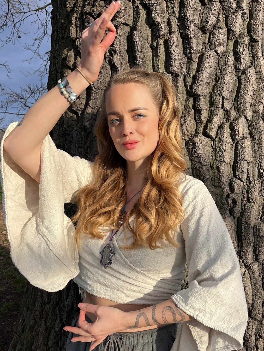 Maia leaning against an oak tree in low golden sun, one hand raised