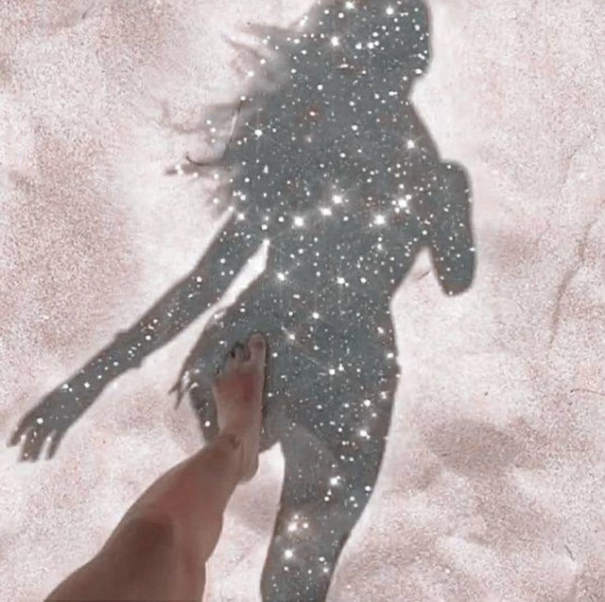 A woman&rsquo;s shadow cast on pale sand, filled with points of light
